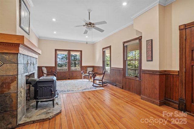 sitting room with ornamental molding, ceiling fan, light hardwood / wood-style floors, and a wood stove