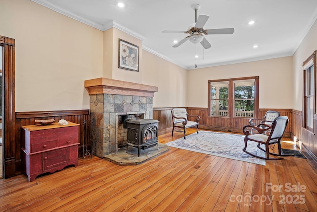 living area with ceiling fan, light hardwood / wood-style flooring, crown molding, and a wood stove