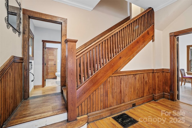 staircase with wood-type flooring, wooden walls, and crown molding