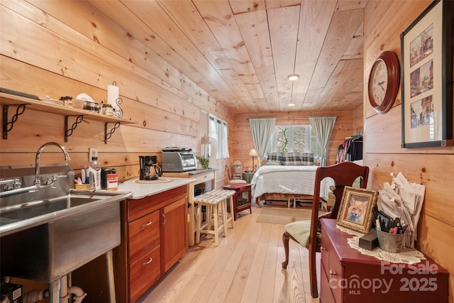 bedroom featuring wood walls, light hardwood / wood-style floors, wooden ceiling, and sink