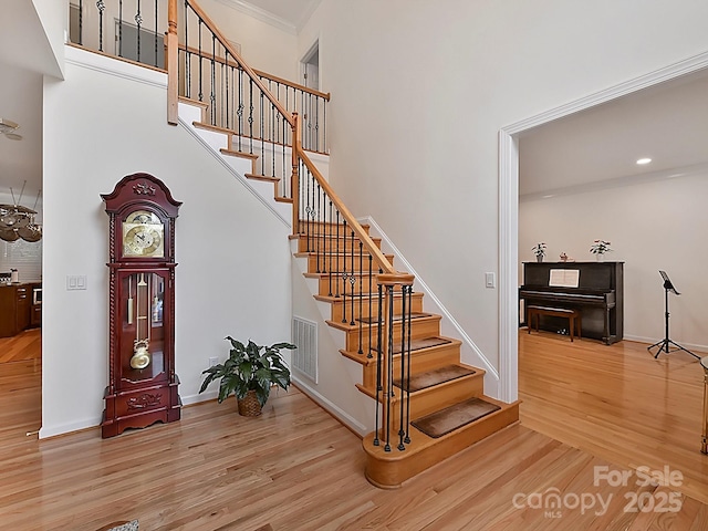 stairs featuring hardwood / wood-style flooring, crown molding, and a high ceiling