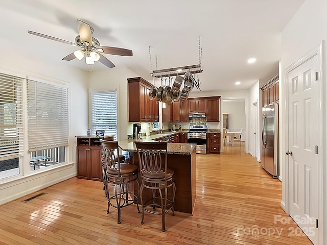 kitchen with a breakfast bar area, light wood-type flooring, kitchen peninsula, ceiling fan, and stainless steel appliances