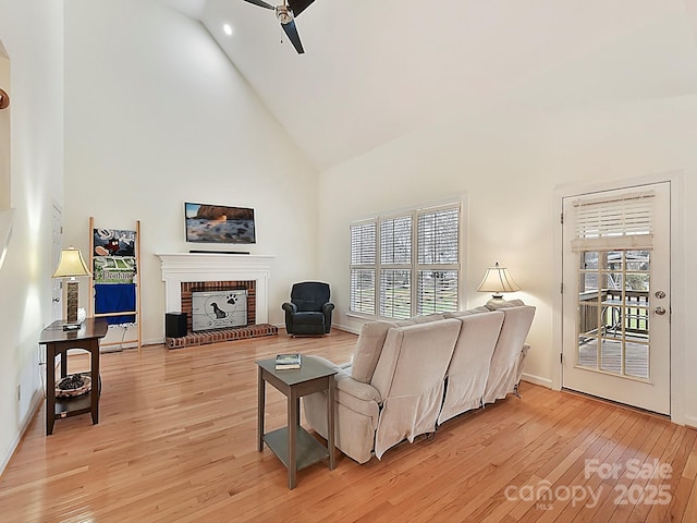 living room with ceiling fan, light wood-type flooring, a fireplace, and high vaulted ceiling