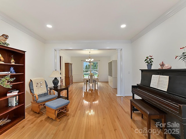 living area featuring decorative columns, crown molding, an inviting chandelier, and light hardwood / wood-style flooring