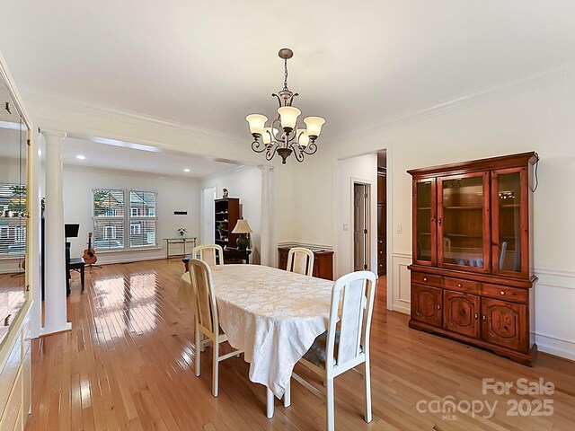 dining space with ornate columns, ornamental molding, light hardwood / wood-style floors, and a notable chandelier