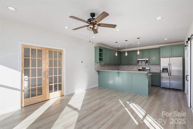 kitchen with tasteful backsplash, kitchen peninsula, green cabinets, hanging light fixtures, and appliances with stainless steel finishes