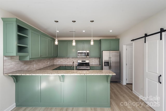 kitchen with a barn door, kitchen peninsula, green cabinets, appliances with stainless steel finishes, and pendant lighting