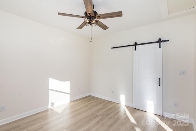 unfurnished room with ceiling fan, light hardwood / wood-style flooring, and a barn door