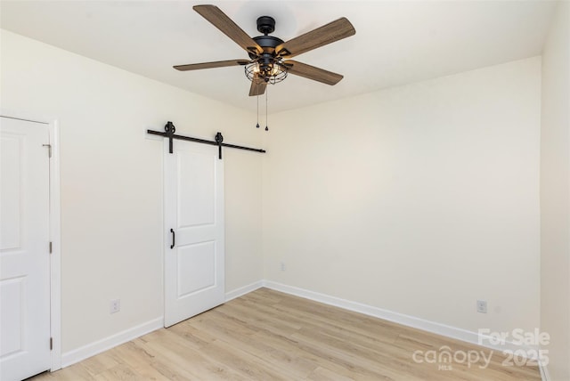 spare room featuring ceiling fan, a barn door, and light hardwood / wood-style flooring