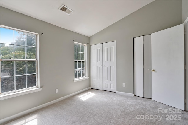 unfurnished bedroom with lofted ceiling, light colored carpet, and multiple closets