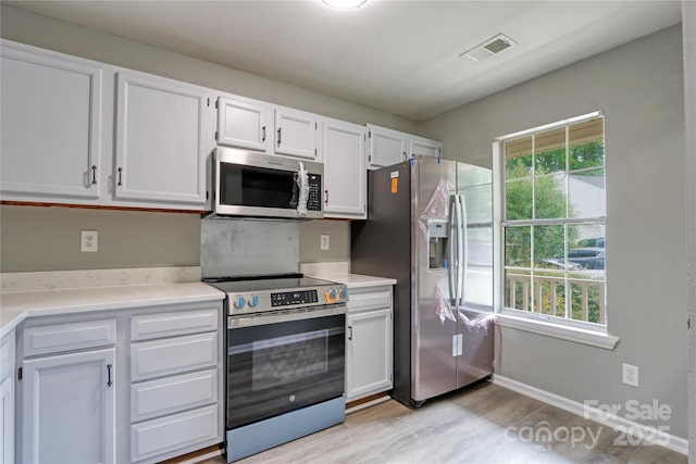 kitchen featuring stainless steel appliances, white cabinets, light wood-type flooring, and a wealth of natural light