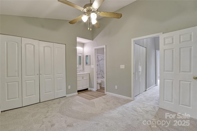 unfurnished bedroom with a closet, ensuite bath, light colored carpet, ceiling fan, and high vaulted ceiling