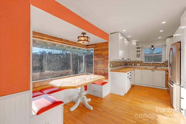 kitchen featuring white cabinetry, sink, backsplash, stainless steel fridge, and light hardwood / wood-style flooring