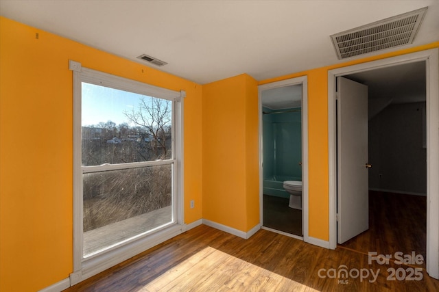 unfurnished bedroom featuring ensuite bath, a walk in closet, a closet, and hardwood / wood-style floors