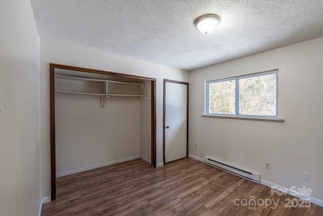 unfurnished bedroom featuring baseboard heating, dark hardwood / wood-style flooring, a closet, and a textured ceiling