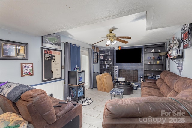 tiled living room with ceiling fan, built in shelves, a large fireplace, and a textured ceiling