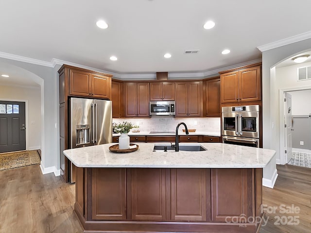 kitchen with light stone counters, appliances with stainless steel finishes, sink, and a kitchen island with sink