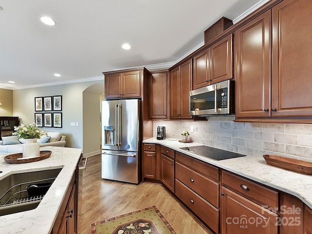 kitchen featuring light stone counters, light wood-type flooring, ornamental molding, stainless steel appliances, and backsplash