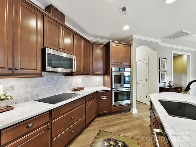 kitchen featuring sink, stainless steel appliances, light stone countertops, light hardwood / wood-style floors, and decorative backsplash