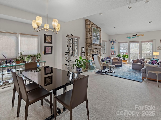 dining room featuring a stone fireplace, vaulted ceiling, carpet flooring, a textured ceiling, and an inviting chandelier