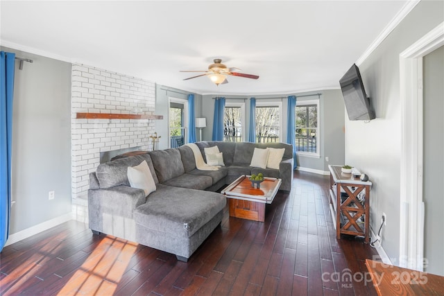 living room featuring dark wood-type flooring, crown molding, a brick fireplace, and ceiling fan