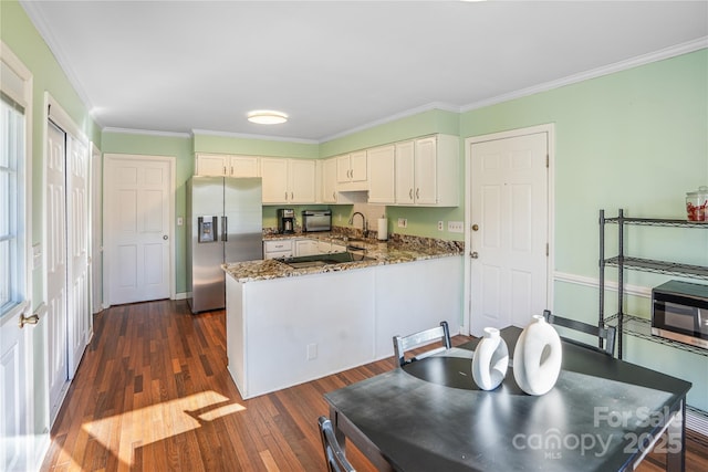 kitchen featuring dark hardwood / wood-style flooring, dark stone counters, stainless steel fridge, kitchen peninsula, and crown molding