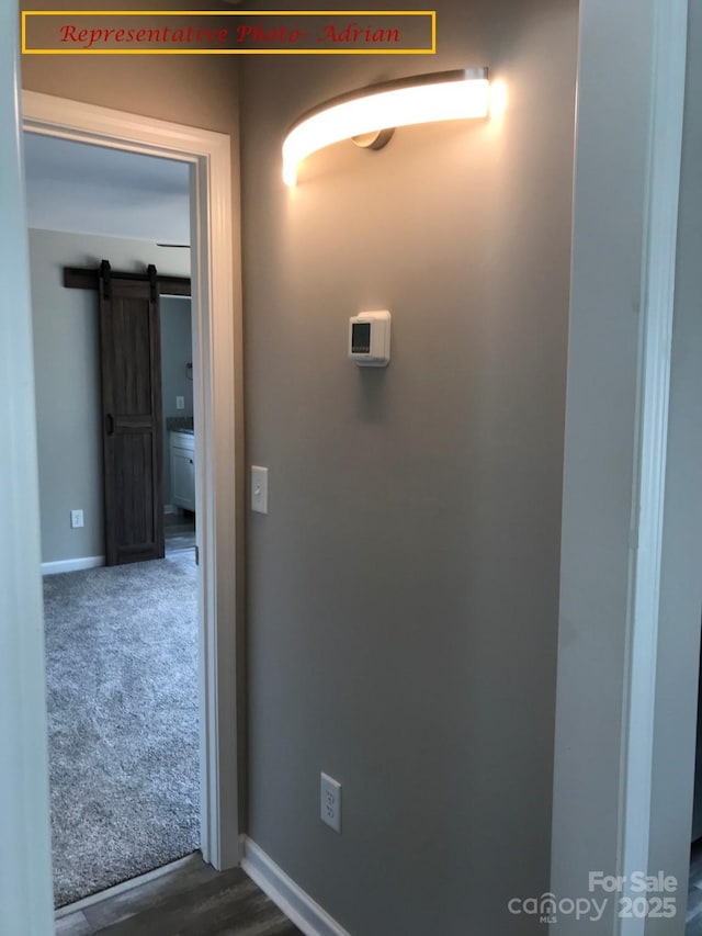 hallway with a barn door and dark colored carpet