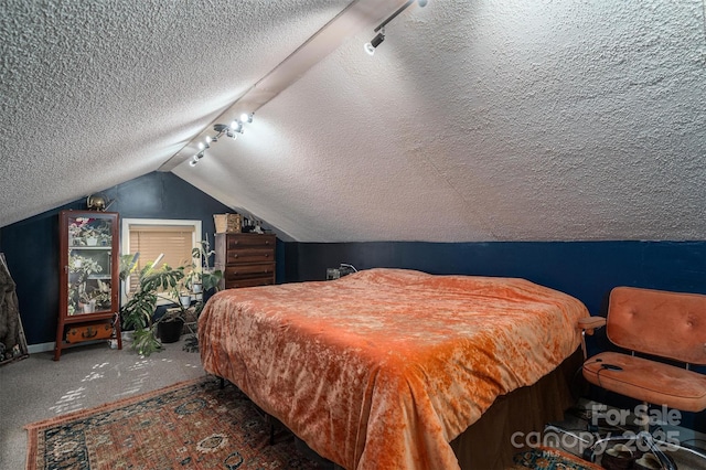 carpeted bedroom with lofted ceiling and rail lighting