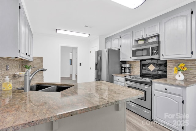 kitchen with appliances with stainless steel finishes, kitchen peninsula, decorative backsplash, and sink