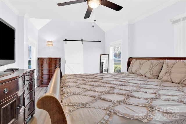 bedroom with lofted ceiling, ornamental molding, ceiling fan, light hardwood / wood-style floors, and a barn door