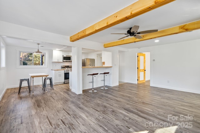 unfurnished living room featuring ceiling fan, beam ceiling, and light wood-type flooring