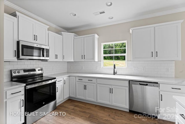 kitchen featuring dark wood-style flooring, appliances with stainless steel finishes, ornamental molding, white cabinetry, and a sink