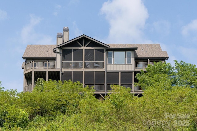 back of property with a sunroom, roof with shingles, and a chimney