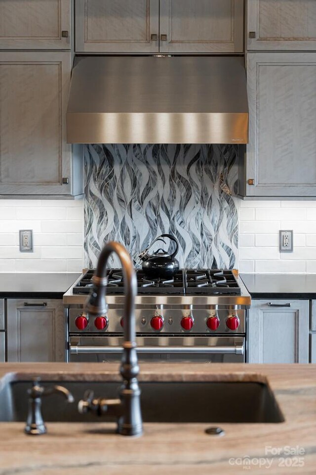 kitchen with light countertops, high end stainless steel range, decorative backsplash, and range hood