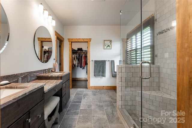 full bath with a sink, a shower stall, baseboards, and double vanity