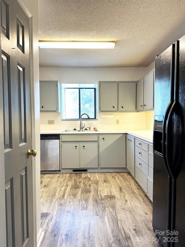 kitchen featuring black fridge with ice dispenser, a textured ceiling, stainless steel dishwasher, light hardwood / wood-style floors, and sink