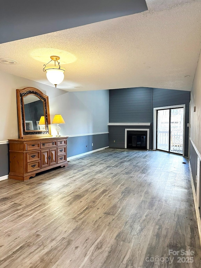 unfurnished living room featuring a fireplace, a textured ceiling, vaulted ceiling, and hardwood / wood-style flooring