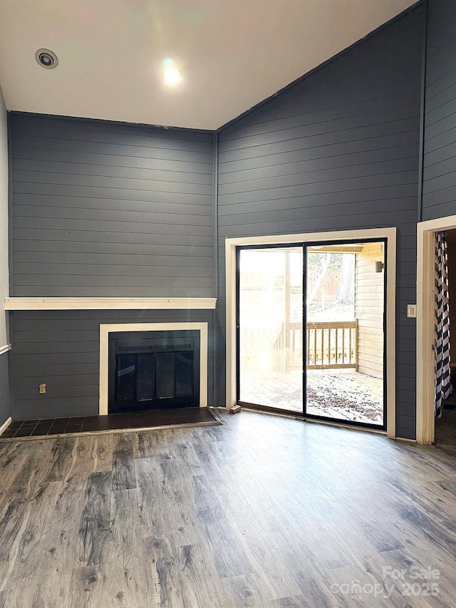 unfurnished living room with hardwood / wood-style floors, high vaulted ceiling, and wood walls