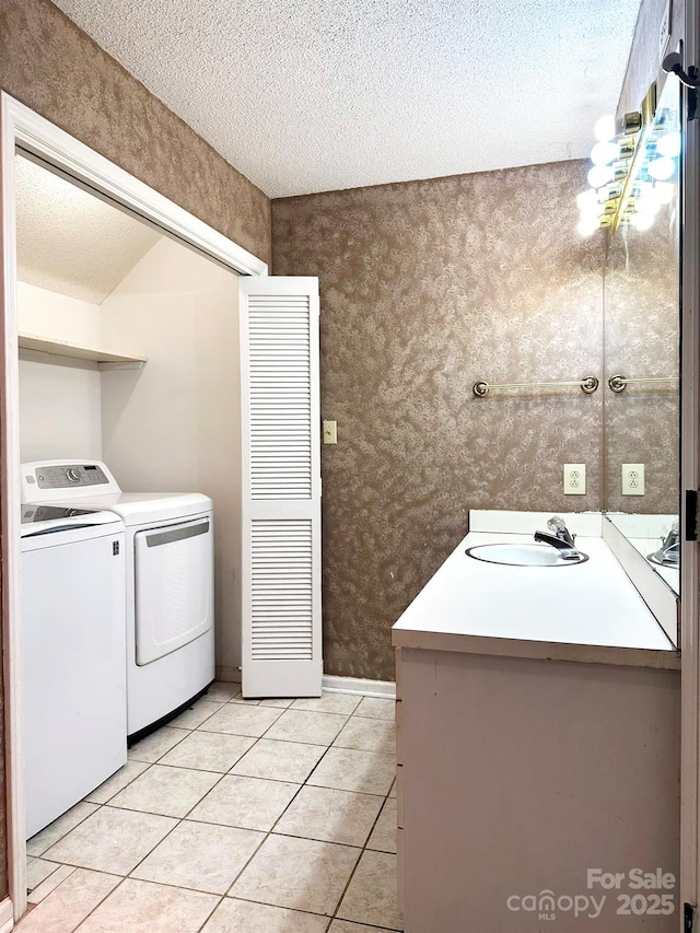 clothes washing area with a textured ceiling, washer and dryer, light tile patterned flooring, and sink