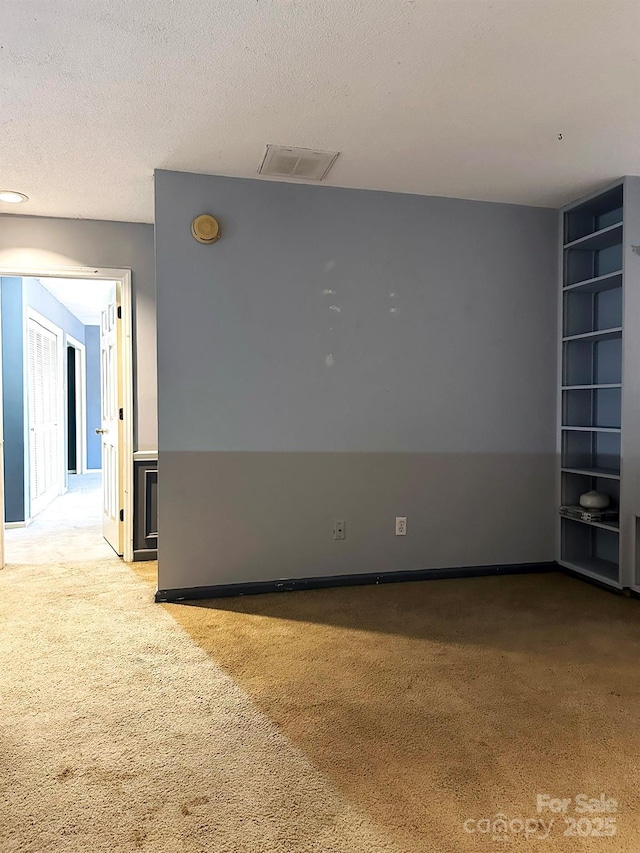 unfurnished room with a textured ceiling, light colored carpet, and built in shelves