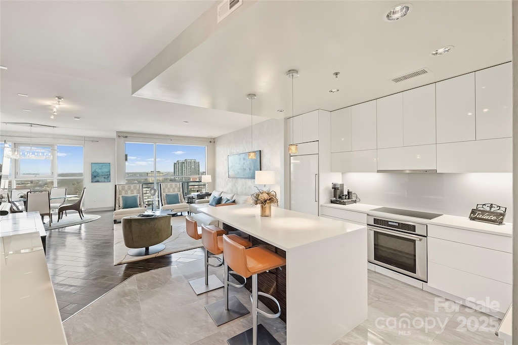 kitchen featuring oven, white cabinetry, pendant lighting, black electric cooktop, and a breakfast bar