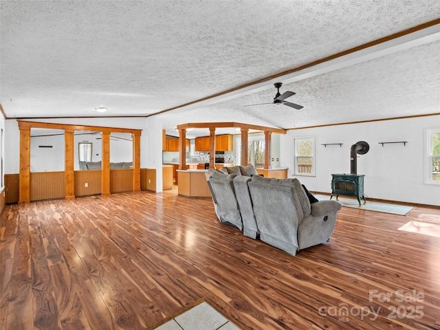 unfurnished living room featuring ceiling fan, wood-type flooring, a healthy amount of sunlight, a wood stove, and a textured ceiling