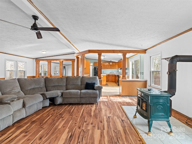 living room with ceiling fan, a wood stove, light wood-type flooring, a textured ceiling, and ornamental molding