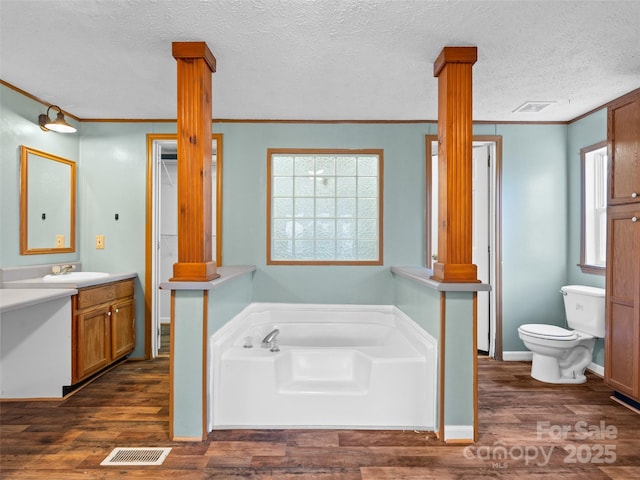 bathroom featuring a textured ceiling, hardwood / wood-style flooring, a tub to relax in, ornamental molding, and decorative columns