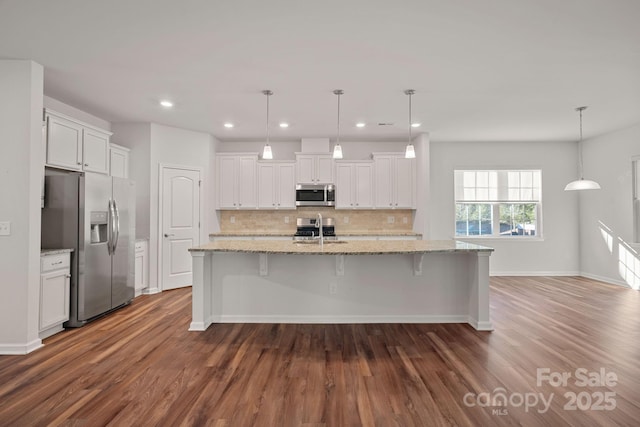 kitchen with white cabinets, hanging light fixtures, stainless steel appliances, light stone countertops, and a center island with sink