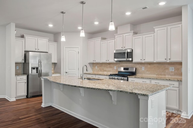 kitchen with sink, a kitchen island with sink, stainless steel appliances, white cabinets, and decorative light fixtures