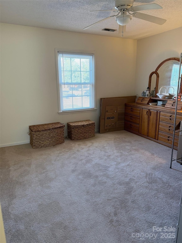 bedroom with ceiling fan, light colored carpet, and a textured ceiling