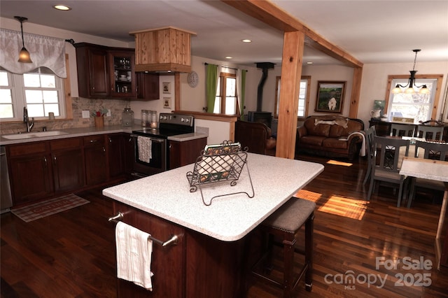 kitchen with sink, hanging light fixtures, dark hardwood / wood-style flooring, stainless steel electric stove, and a wood stove