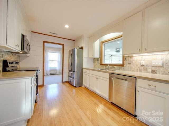 kitchen with appliances with stainless steel finishes, decorative backsplash, white cabinets, light hardwood / wood-style flooring, and sink