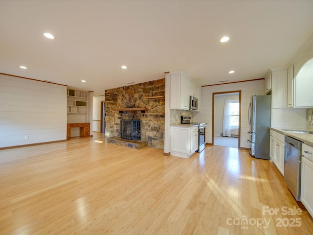 kitchen featuring white cabinets, light wood-type flooring, a fireplace, and stainless steel appliances